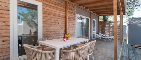 A covered outdoor area with a table and chairs, a glass door, and a wooden deck.