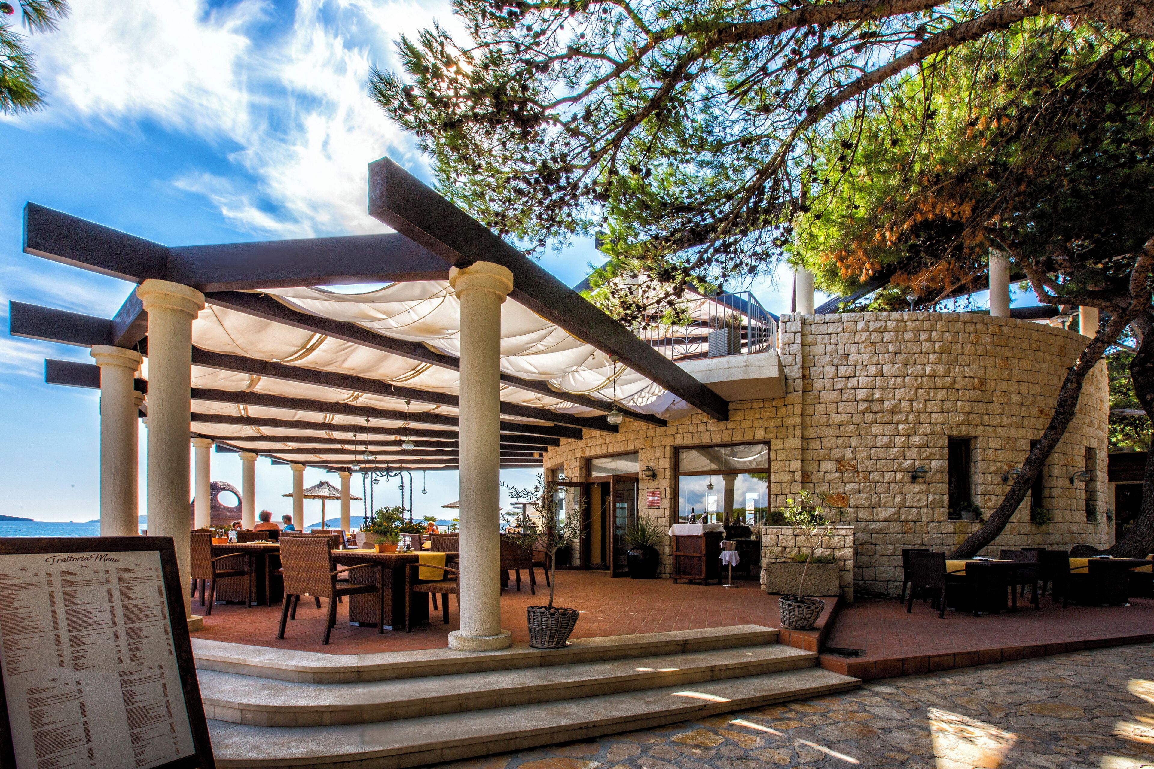 An outdoor dining area with stone walls, tables, and chairs under a pergola.