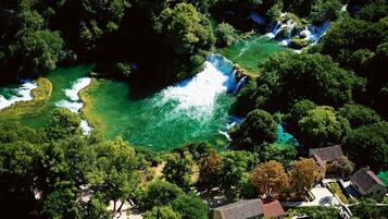 Una vista aerea di una zona lungo il fiume con una cascata, vegetazione lussureggiante e edifici tradizionali con tetti in tegole rosse.