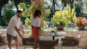 Patio esterno con sedie in vimini, un tavolo e piante in vaso.