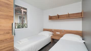 Una habitación con dos camas individuales, un armario de madera, una ventana con vistas a zonas verdes y un estante sobre las camas.