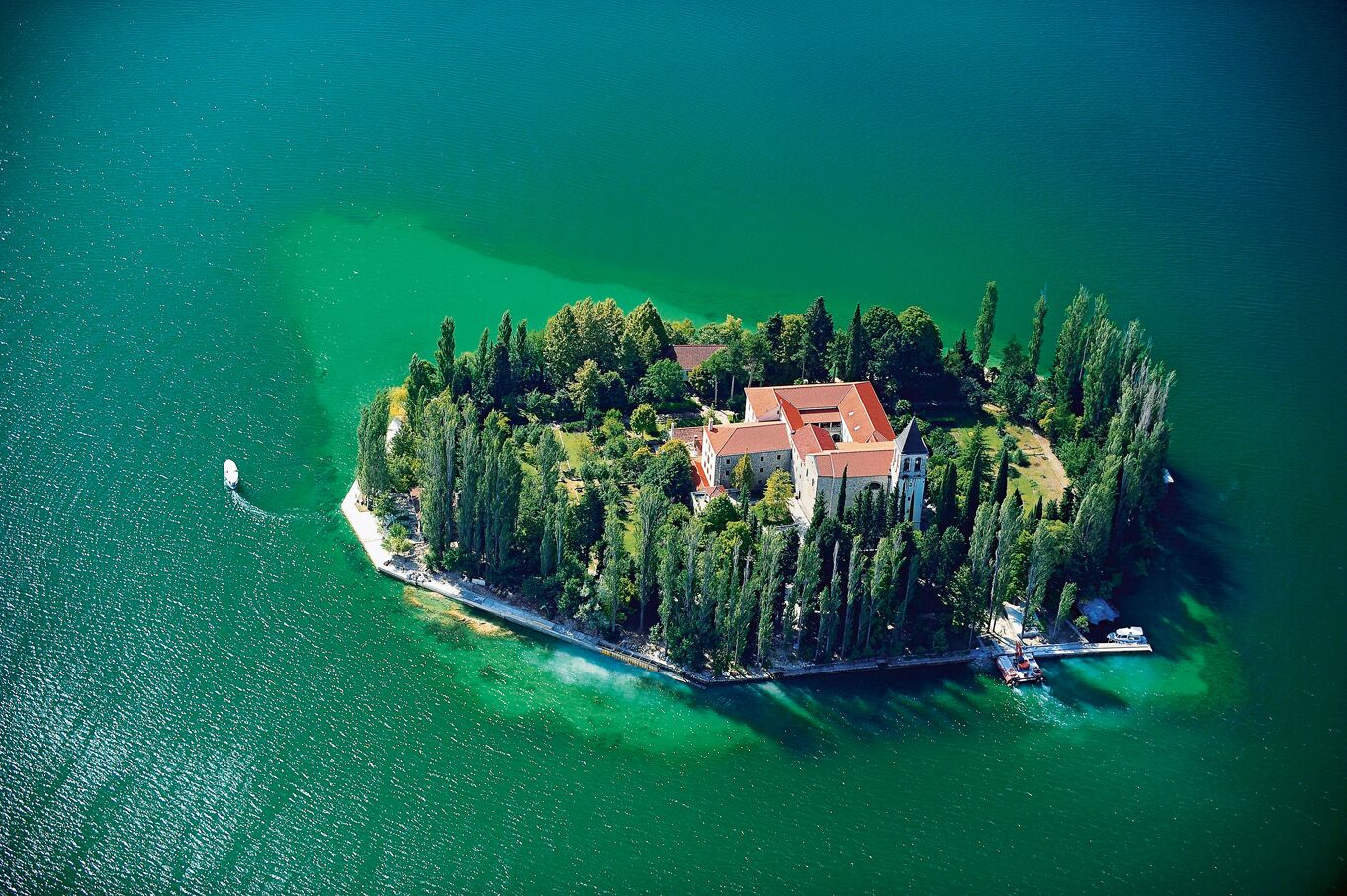 Une vue aérienne d’une île isolée, avec un bâtiment central entouré d’une végétation dense, le tout relié par une étroite route.