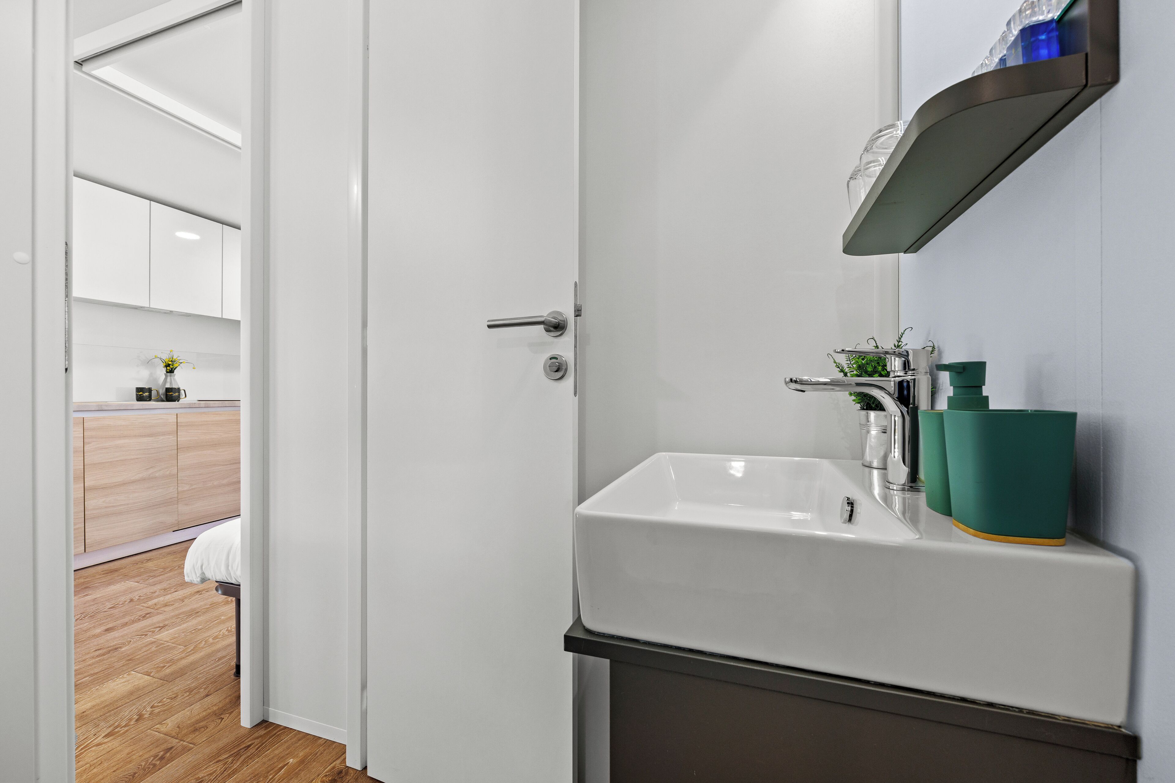 Un baño moderno con lavamanos blanco, un espejo y una repisa con artículos de aseo.