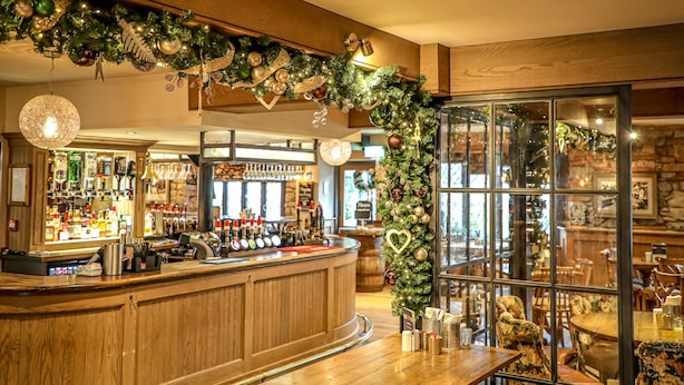 A bar area with wooden counter, bar stools, and Christmas decorations. - Pooley Bridge Inn (Penrith)