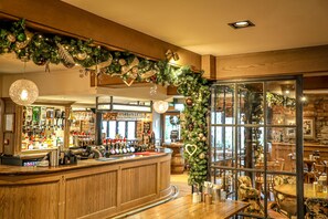 A bar area with wooden counter, bar stools, and Christmas decorations. - Pooley Bridge Inn (Penrith)