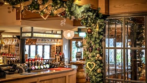 A bar area with a Christmas tree decorated with ornaments and lights. There are shelves with bottles and glasses, and a counter with a cash register. - Pooley Bridge Inn (Penrith)
