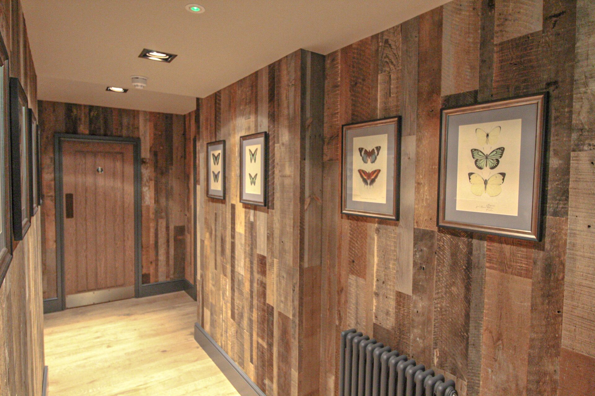 A hallway with wooden paneling and framed butterfly artwork on the walls.