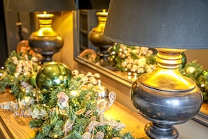 A lamp with a black shade and a gold base, placed on a wooden surface with a Christmas decoration. - Pooley Bridge Inn (Penrith)