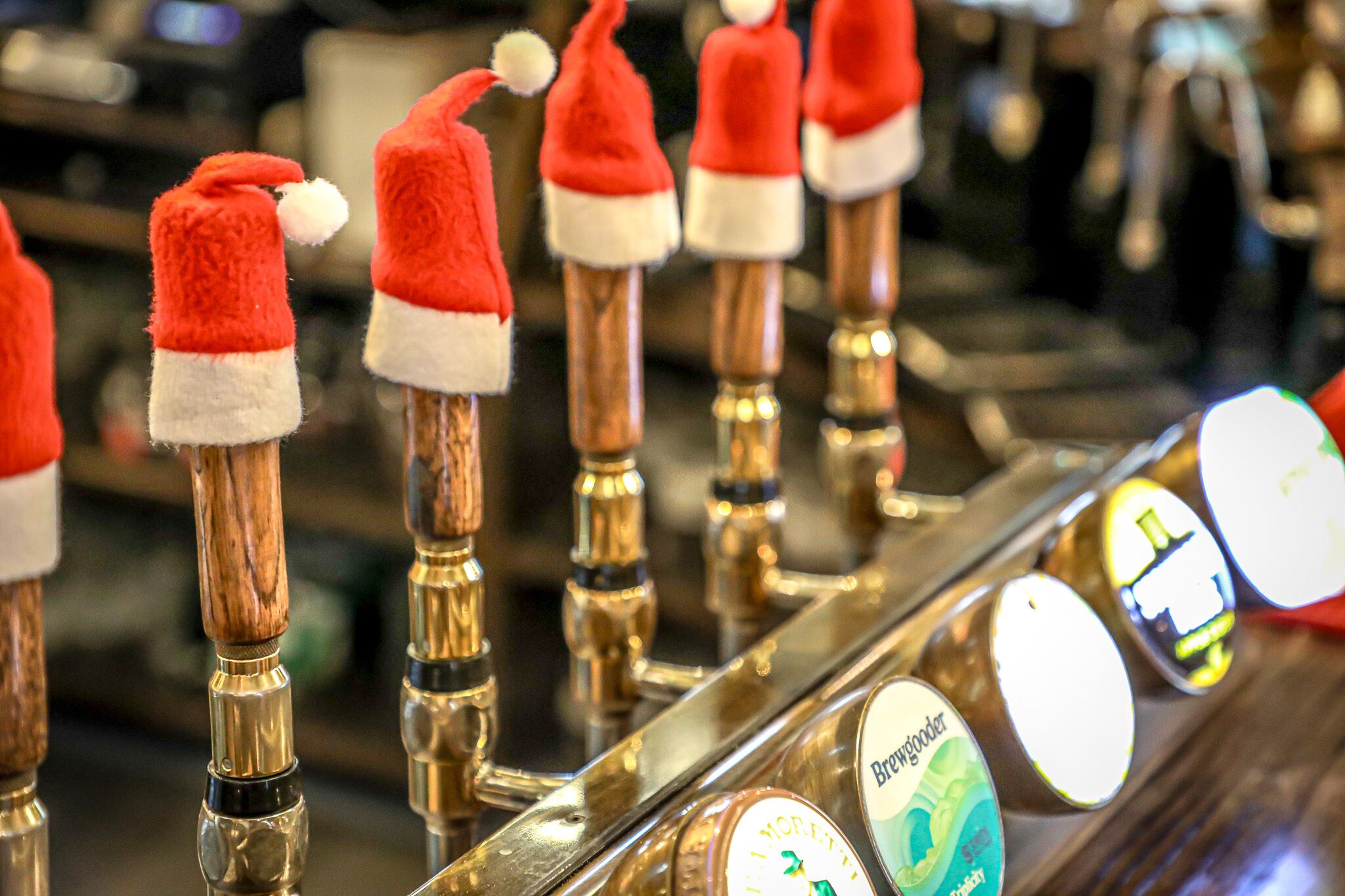 A bar with multiple taps, each topped with a Santa hat.