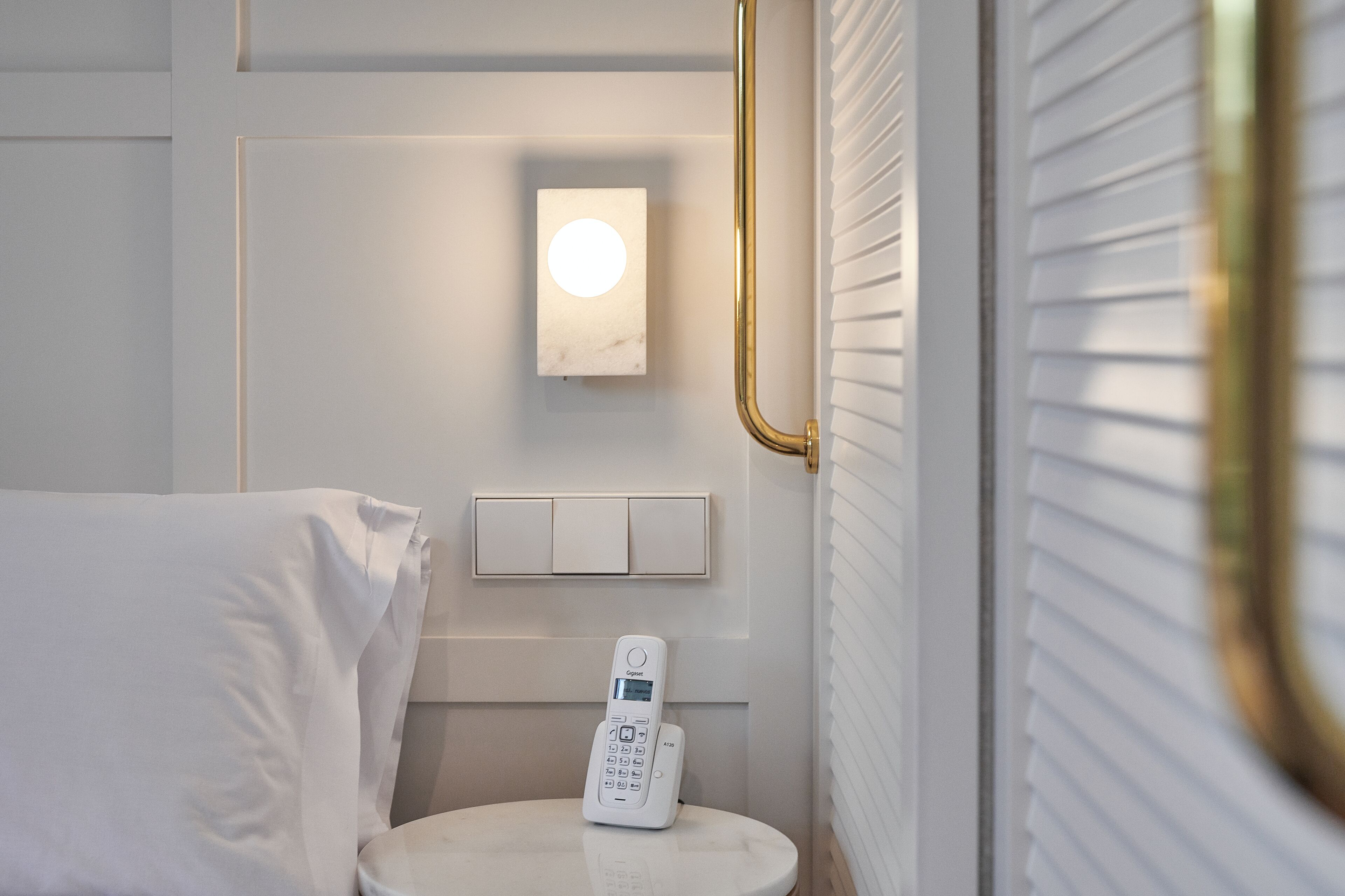Een moderne badkamer met een wit toilet, een nachtkastje met een afstandsbediening, een wandlamp en een gouden leuning.