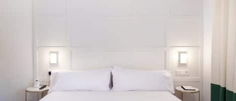 A hotel room with a large bed, two bedside tables, and two wall-mounted lamps.