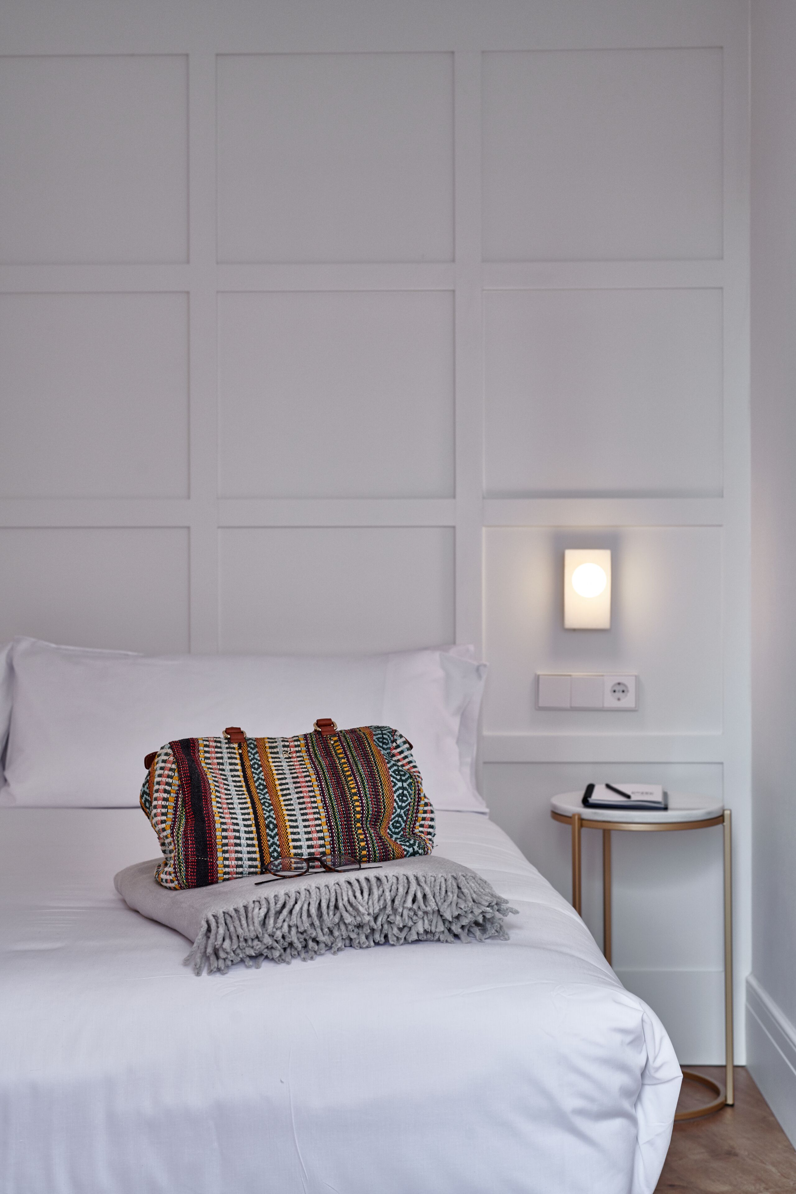 A neatly made bed with a patterned throw pillow and a small bedside table with a lamp.