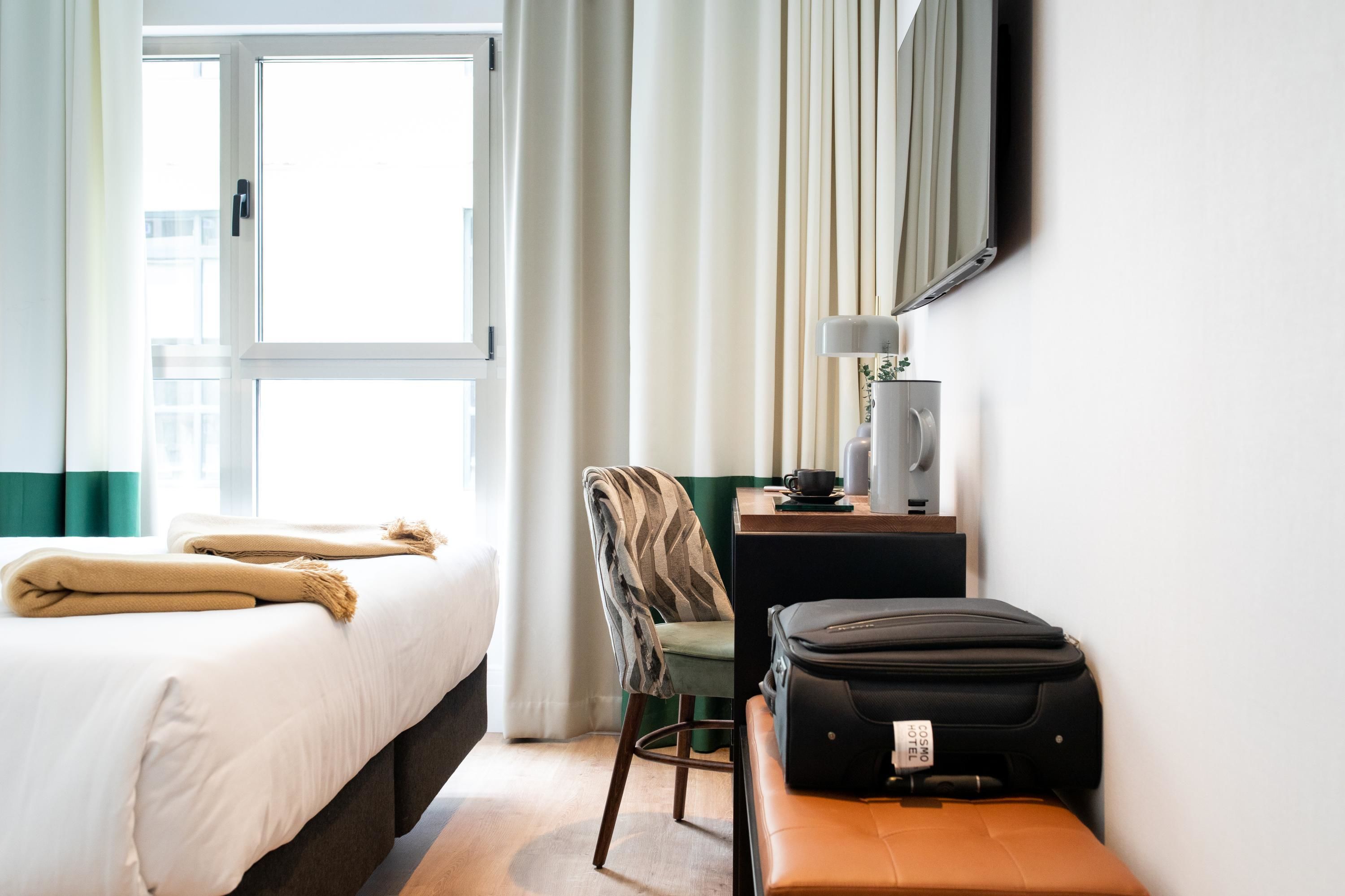 Een hotelkamer met een bed, een bureau, een stoel, een lamp en een koffer.