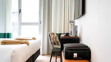 A hotel room with a bed, a desk, a chair, a lamp, and a suitcase.