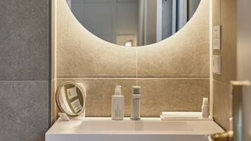A modern bathroom with a round mirror, white sink, and towel rack.