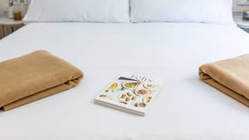 A neatly made bed with white bedding and two brown towels placed on either side of a book titled "Félix" with food images.