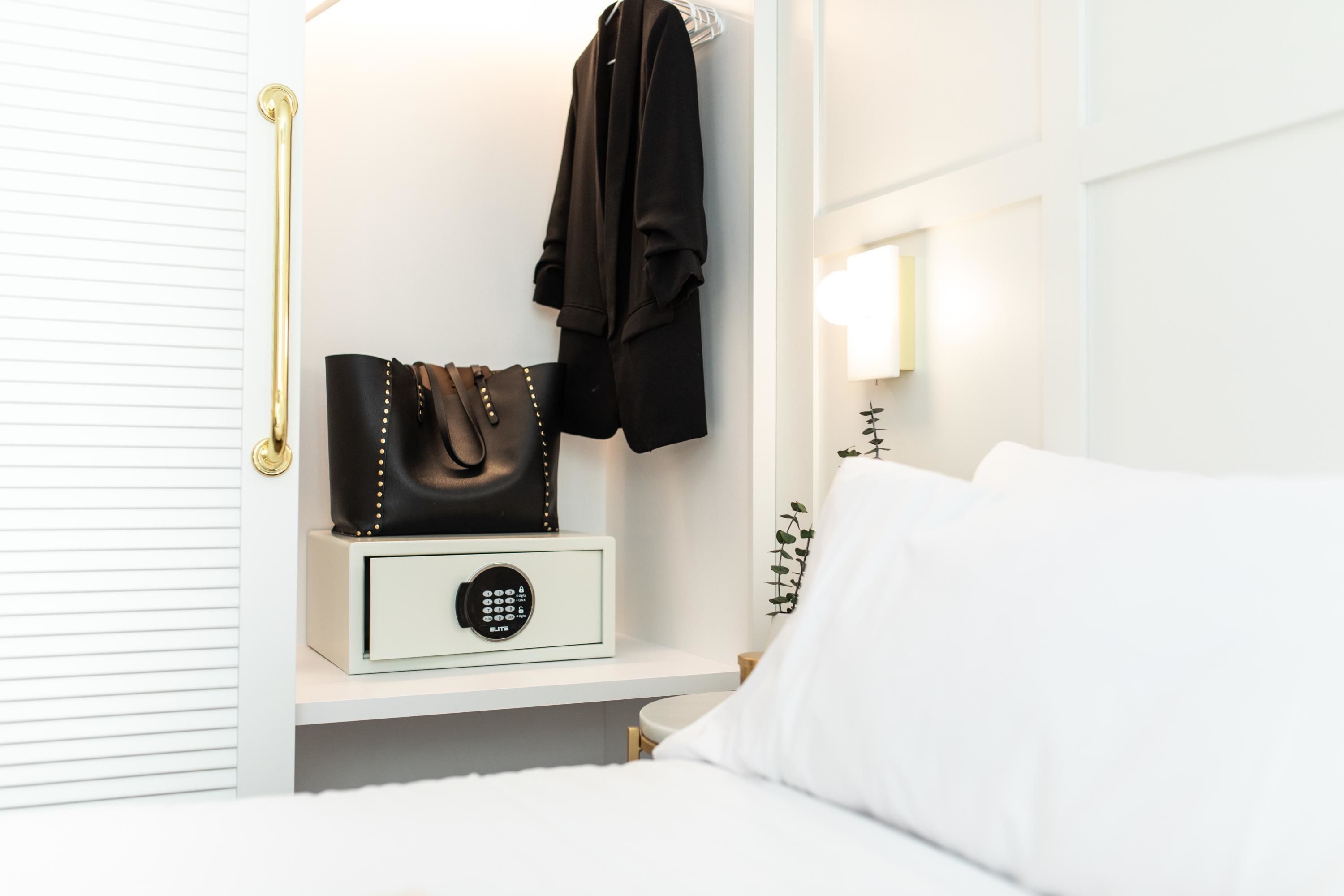 A neatly organized bedroom with a bedside table, a lamp, a bed, and a coat rack.