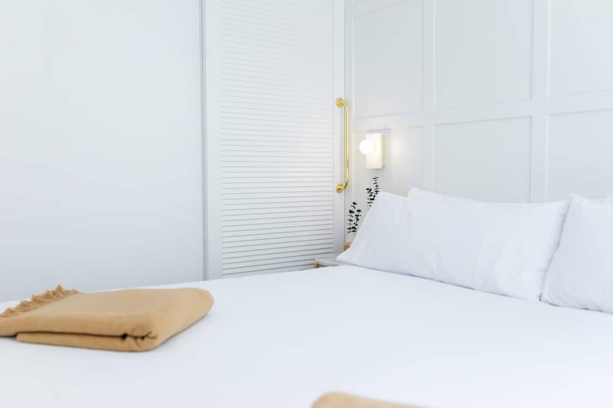 Una habitación blanca con una cama, una mesita de noche y un armario blanco.