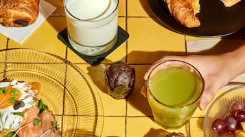 Desayuno con cruasanes, un vaso de leche, una bebida verde y un plato de fruta.