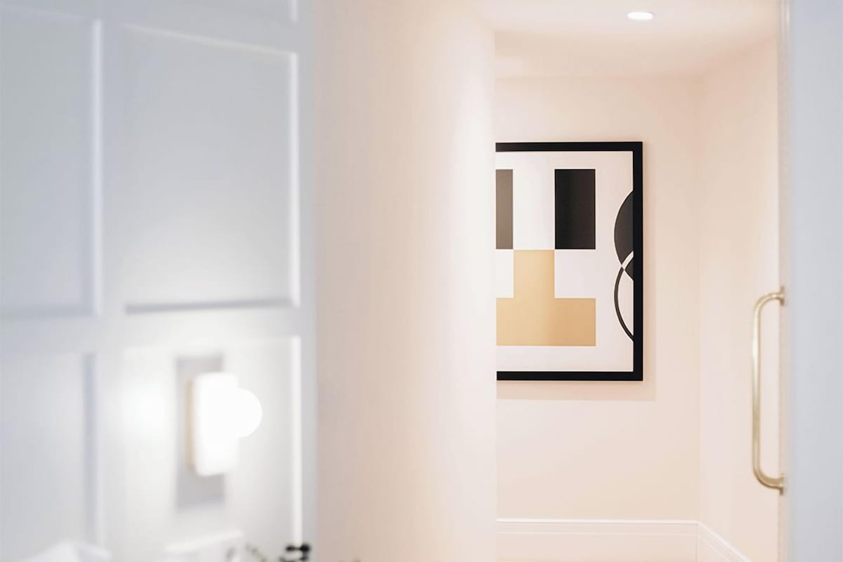 Una habitación de hotel moderna con cama, mesita de noche, lámpara y una obra de arte abstracta enmarcada en la pared.