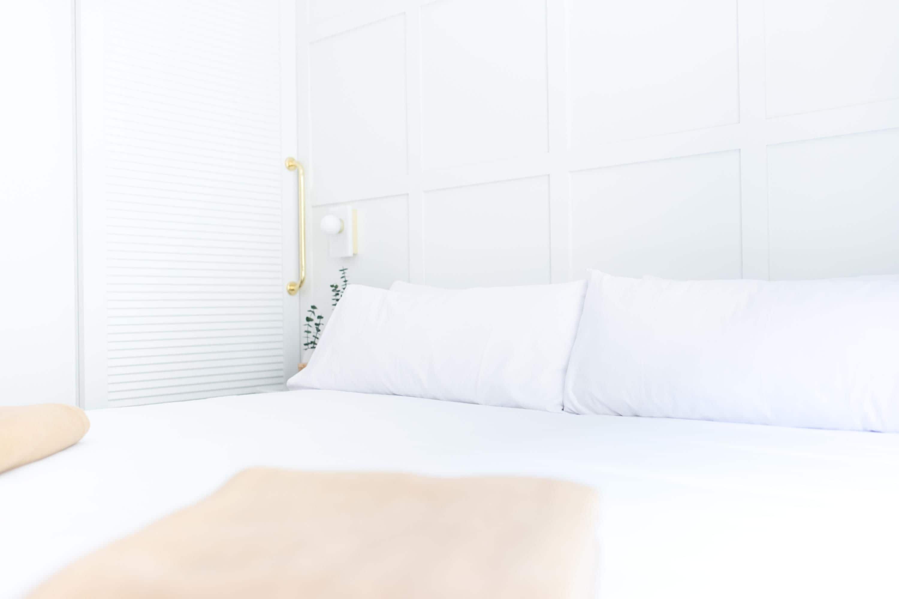 A neatly made bed with white bedding and a beige throw pillow.