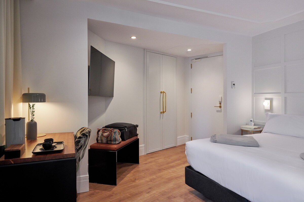 Una habitación de hotel con cama, mesita de noche, lámpara y armario.