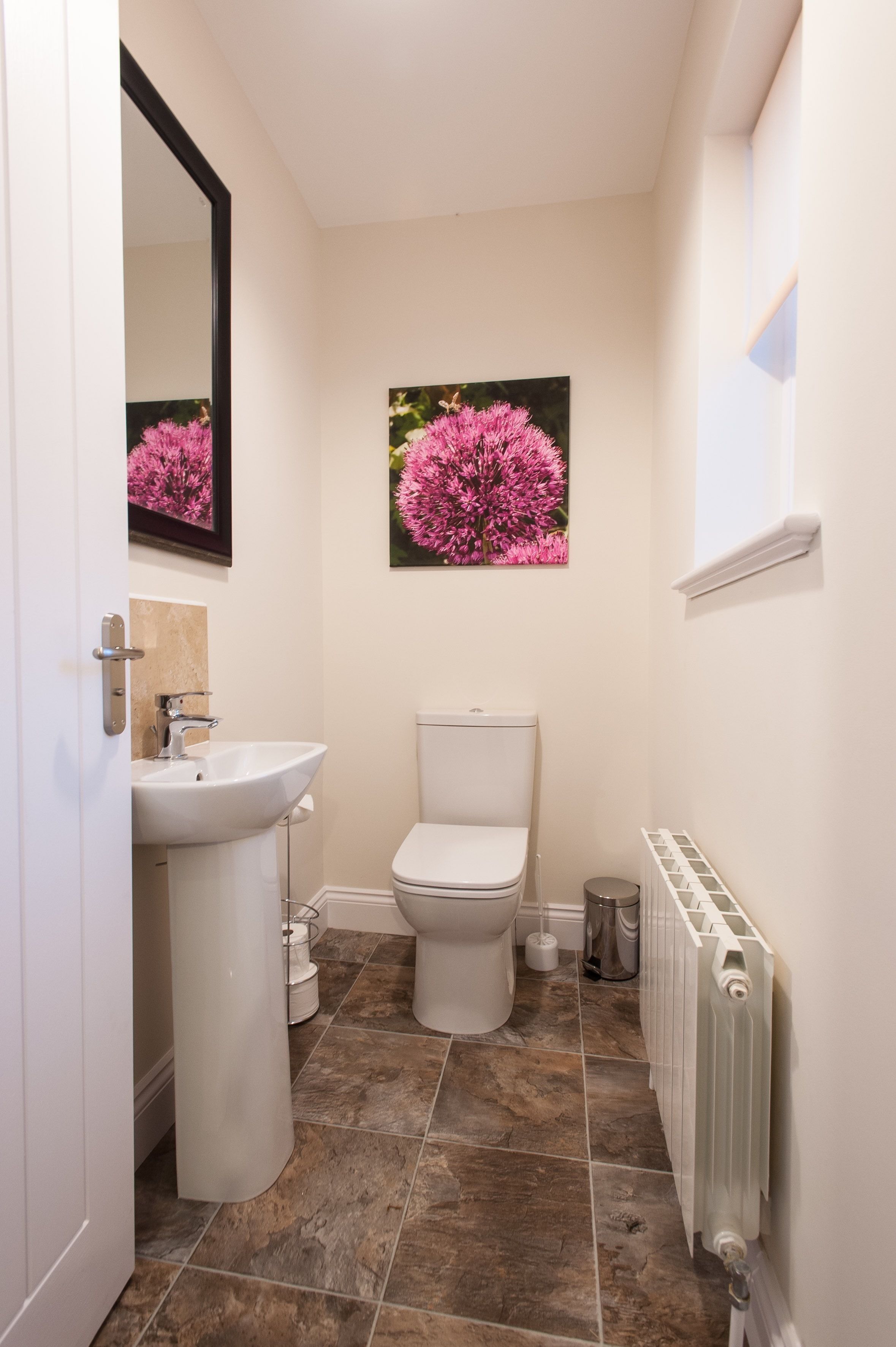 Une petite salle de bain avec un lavabo blanc, des toilettes et un radiateur. Deux tableaux encadrés représentant des motifs floraux sont accrochés au mur.