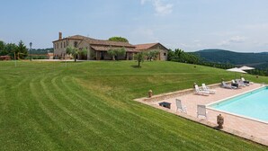 Une grande maison avec une piscine, entourée d’une pelouse bien entretenue et d’arbres.