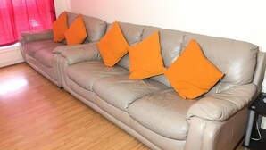 A grey leather sofa with four orange cushions, a wooden floor, and a red curtain.