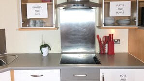 A kitchen with a stainless steel range hood, a sink, and cabinets labeled for glasses, cups, plates, bowls, pots, and pans.