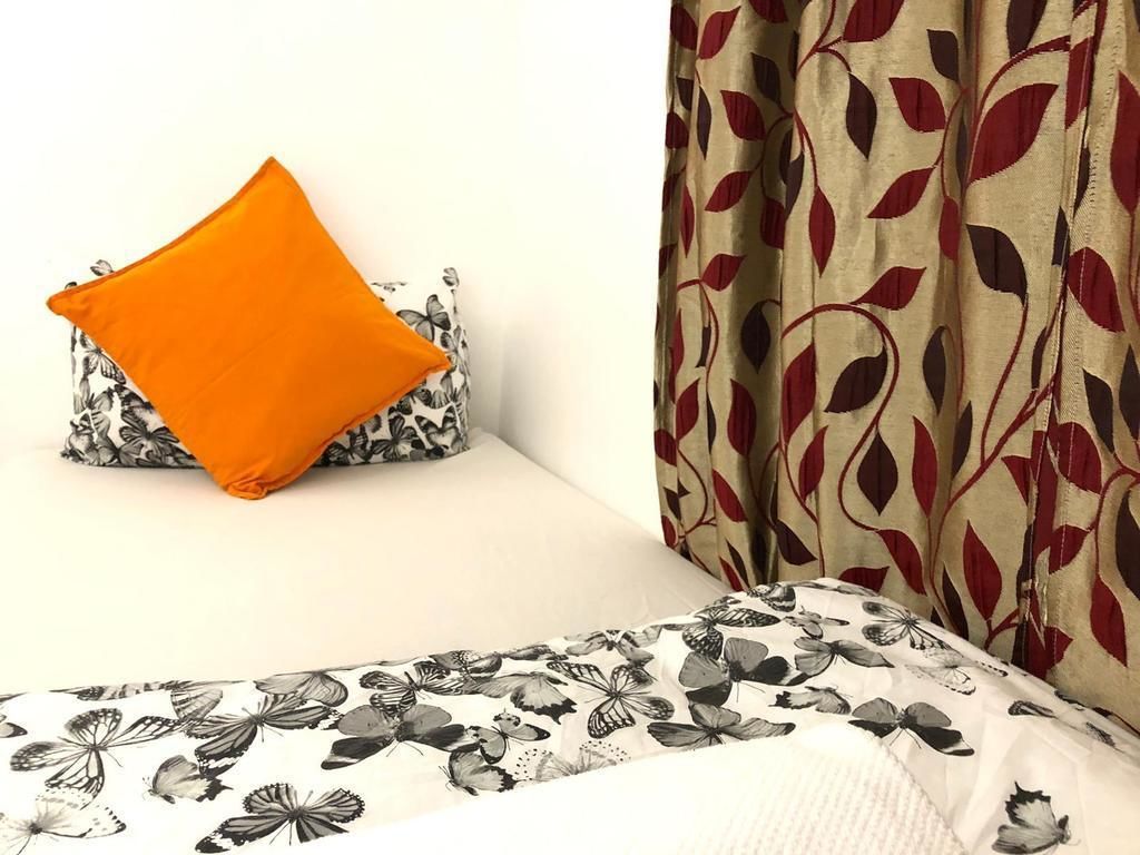 A bed with a floral-patterned bedspread, a pillow with a black and white butterfly design, and a curtain with a red leaf pattern.