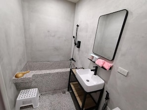 Une petite salle de bain avec un lavabo blanc, un miroir, un espace douche et une petite étagère sur laquelle est posée une serviette rose.