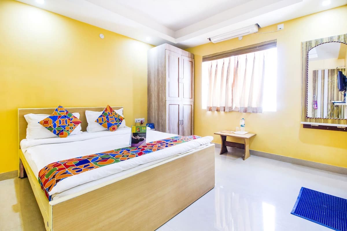A hotel room with a bed, a small table, a mirror, and a window with curtains.