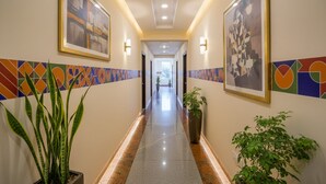 A hotel hallway with framed artwork on the walls, potted plants, and a tiled floor. - FabHotel Amaltas (Ranchi)