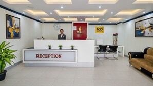 A hotel reception area with a reception desk labeled "RECEPTION," a clock, and a sign for "fab hotels." - FabHotel Amaltas (Ranchi)
