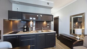 A modern kitchen with dark cabinetry, a stainless steel sink, and a built-in stove. There is a dining table with a chair, and a mirror above the sink. - Pegaz Apartments by Baltic Home (Swinoujscie)