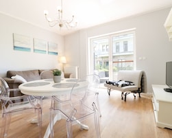 A modern living room with a round glass table, clear chairs, a sofa, and a TV.