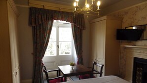 A room with a bed, a table with chairs, a television, and a fireplace. - Ryvington Apartments (Abergavenny)