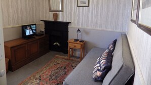 A living room with a fireplace, a television, a sofa, and a small wooden side table. - Ryvington Apartments (Abergavenny)