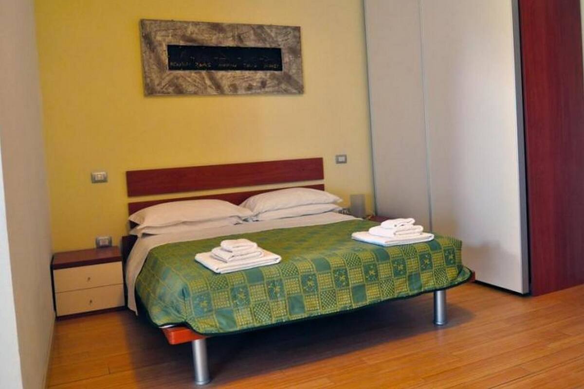 A single bed with a green patterned bedspread, two pillows, and a folded towel on the footboard.