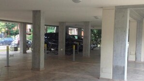 An indoor parking area with concrete pillars, a tiled floor, and bicycles parked in the background. - Residence Rivaverde (Ravenna)