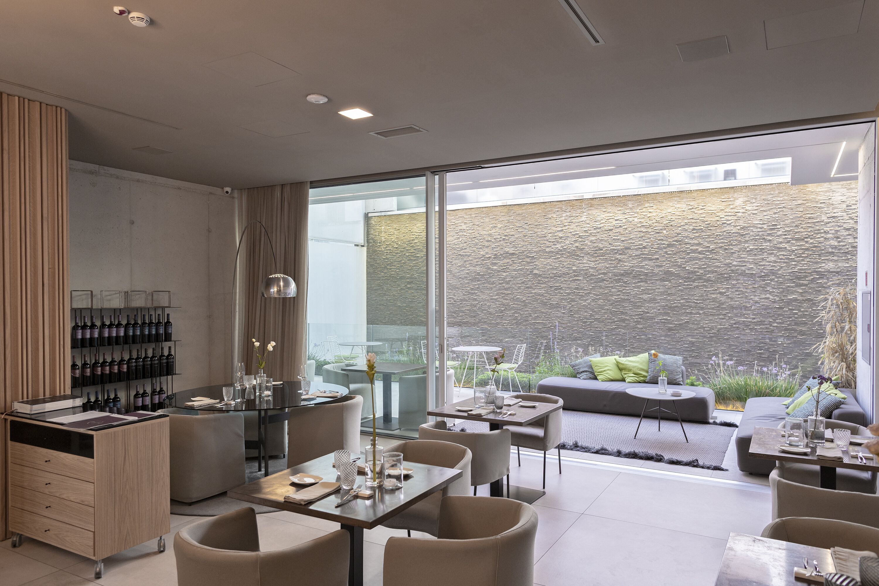 A modern dining area with a wine rack, seating, and a view of the outdoor garden.