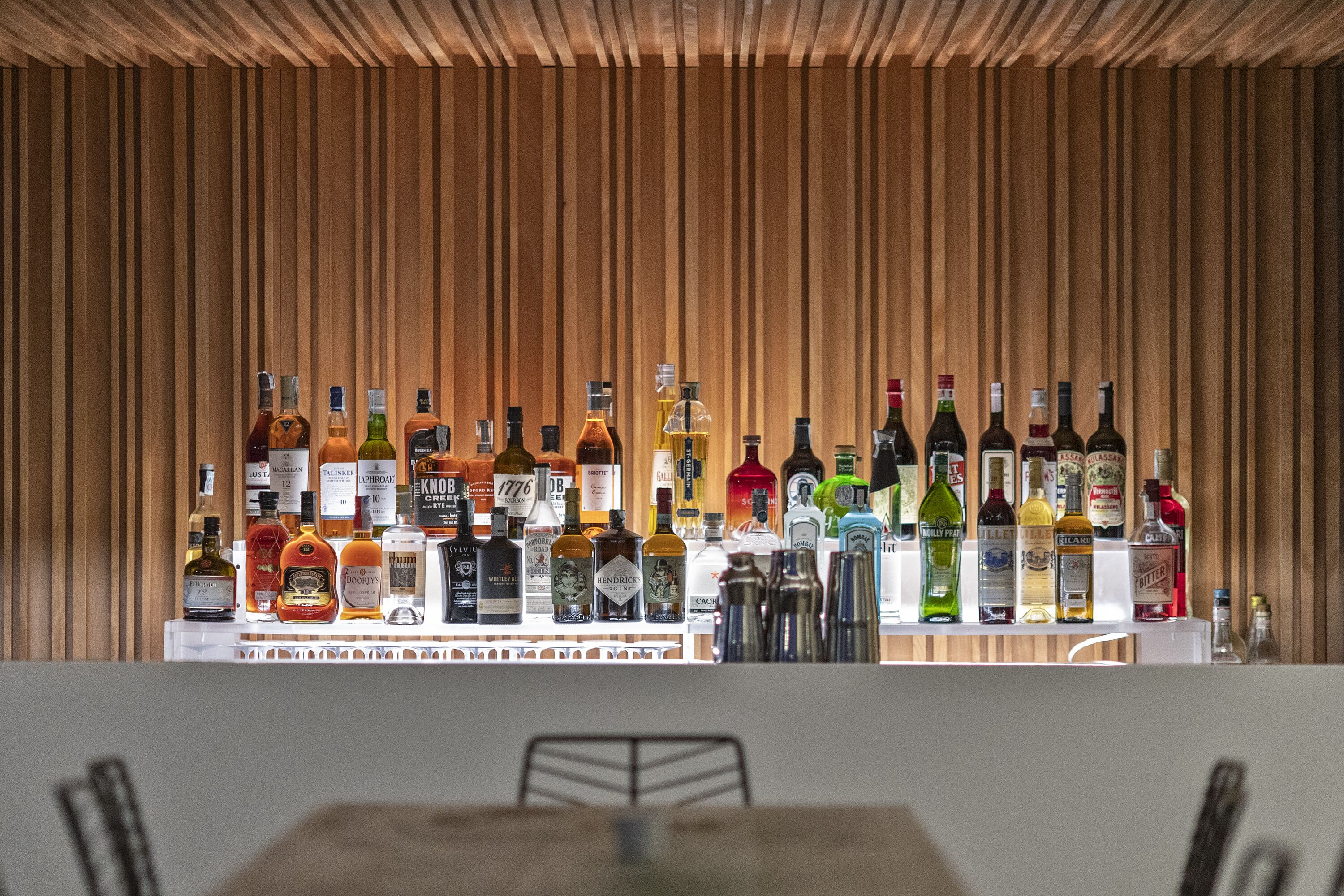 Eine Bar mit einer Auswahl an Spirituosenflaschen, präsentiert auf Regalen vor einem Holzhintergrund.