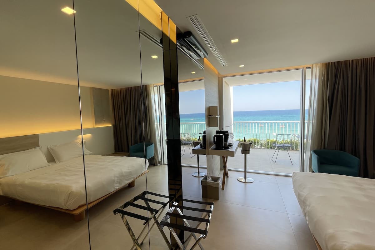 Ein Hotelzimmer mit Balkon, einem Bett, einem Schreibtisch mit Kaffeemaschine und Blick auf den Ozean.