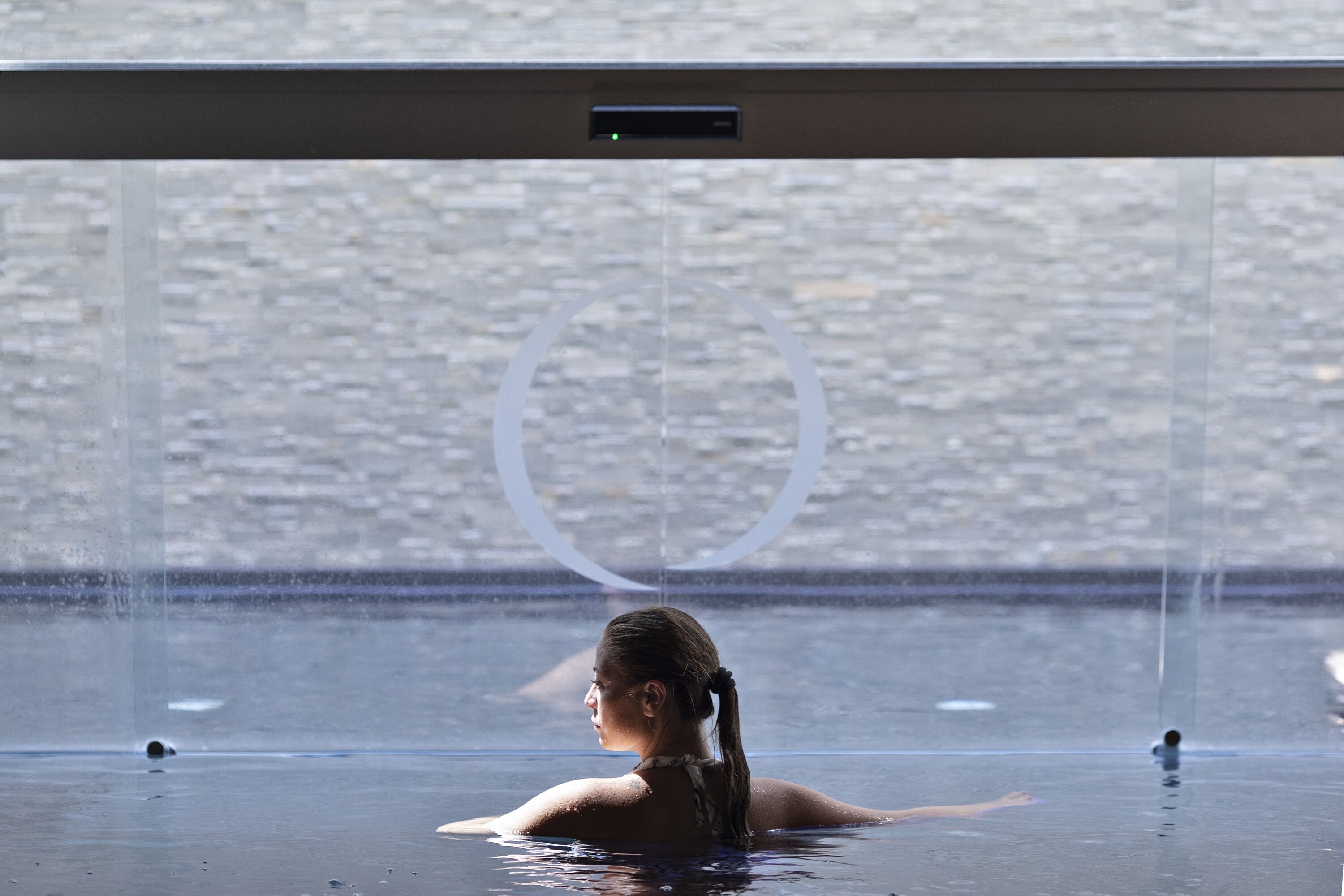 A person in a clear, indoor swimming pool with a view of a rocky landscape through a large window.