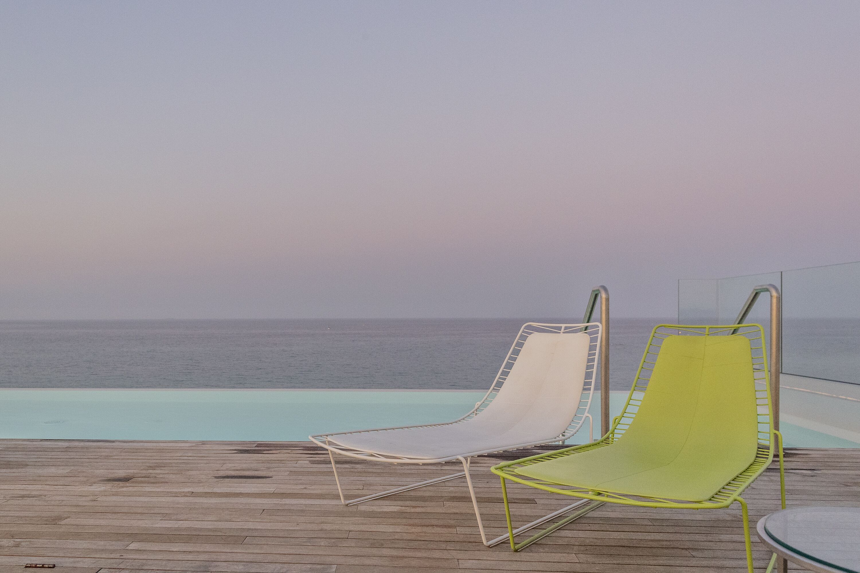 Two lounge chairs by a poolside with a view of the ocean.