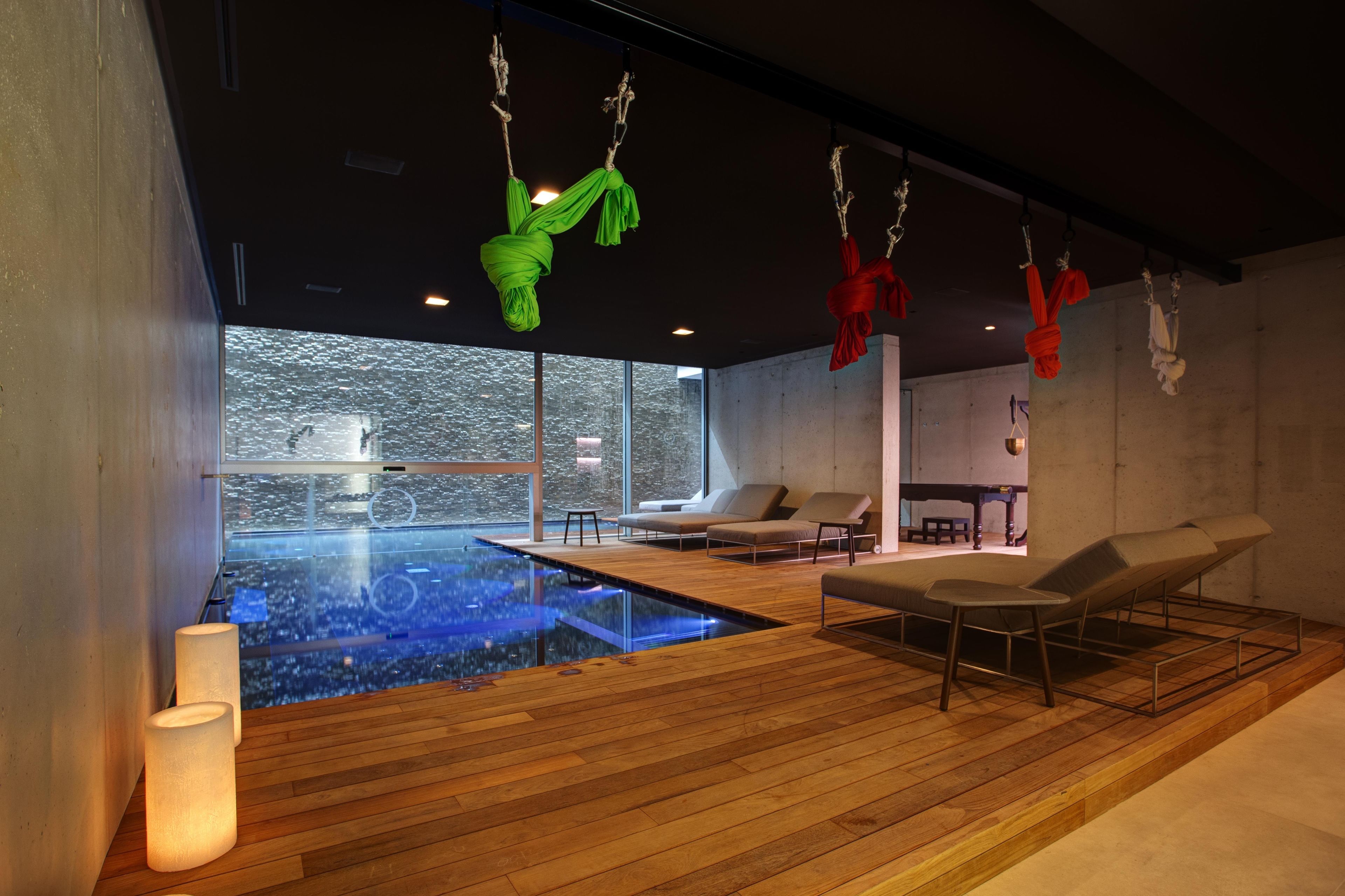 A modern spa with a glass-enclosed infinity pool, wooden flooring, and lounge chairs.
