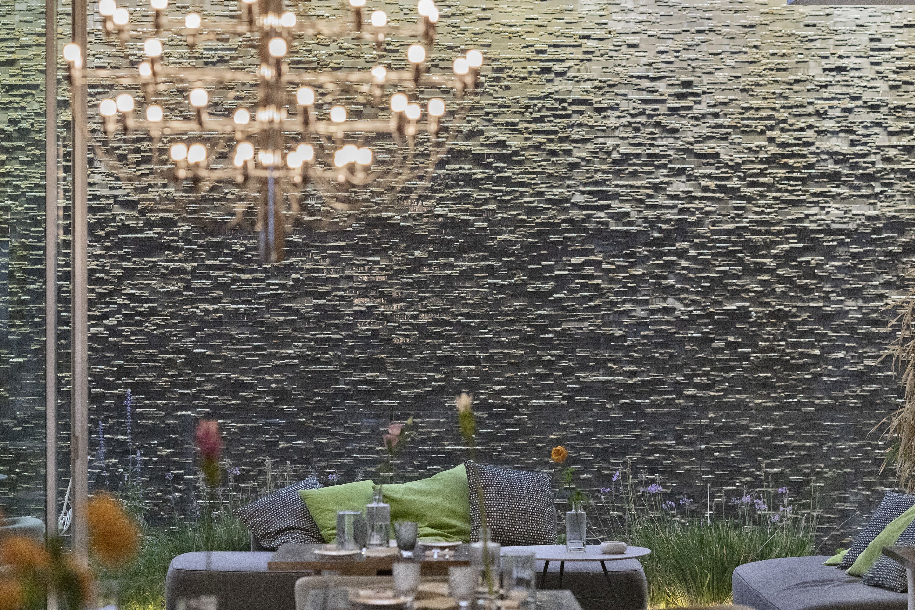 A dining area with a modern chandelier, a patterned wall, and a table set with glasses and a vase.