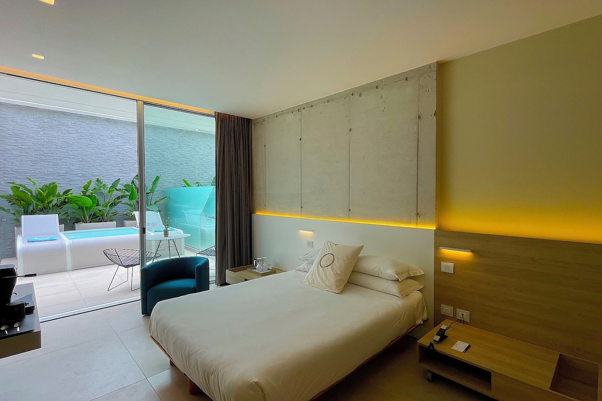 Ein modernes Hotelzimmer mit einem großen Bett, einem Schreibtisch und Meerblick durch raumhohe Fenster.