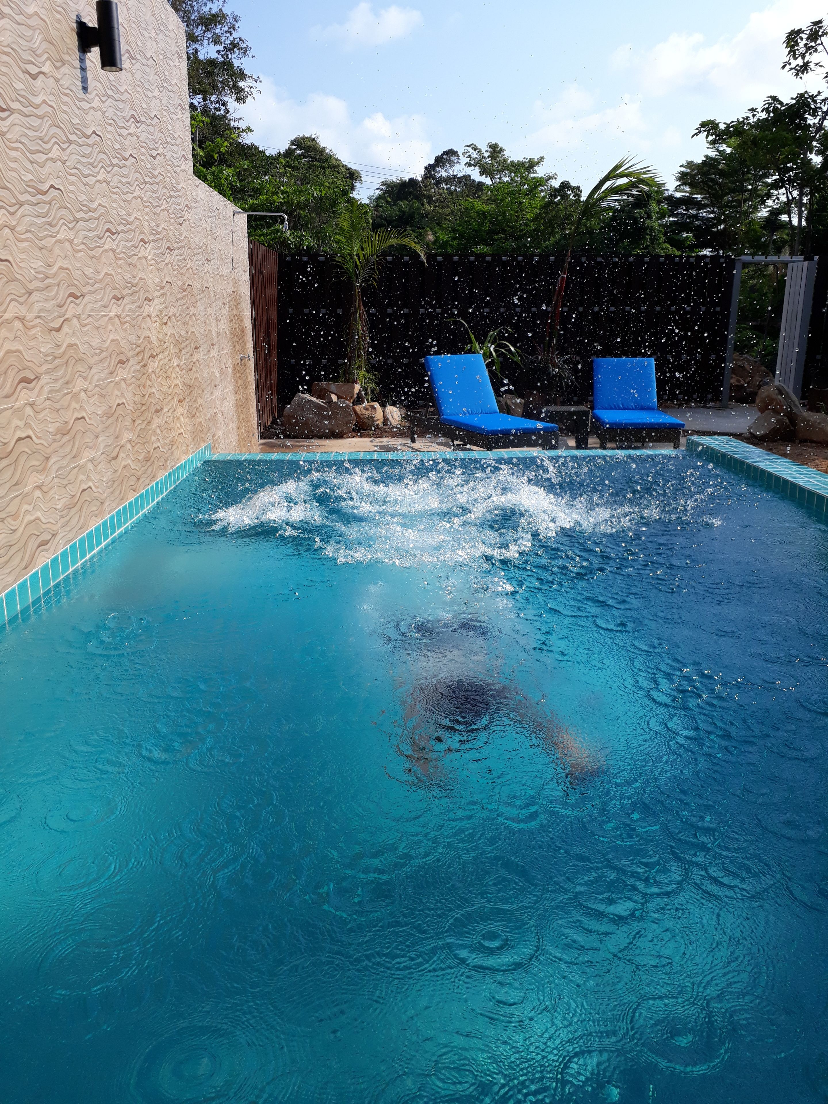 A swimming pool with clear blue water, two blue lounge chairs, and a stone wall.